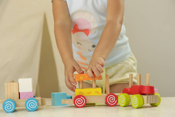 Κορίτσι μικρό παιδί παίζει με ξύλινο τρένο κατασκευασμένο από ξύλινα μπλοκ - εκπαιδευτικά παιχνίδια για νηπιαγωγείο και νηπιαγωγείο.  - Φωτογραφία, εικόνα