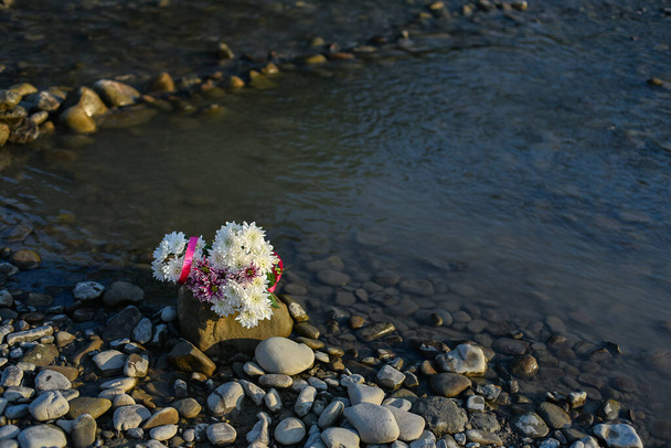 квіти біля річки, букет квітів на кам'яному узбережжі, букет квітів у воді, фотографія букета на заході сонця у воді
 - Фото, зображення