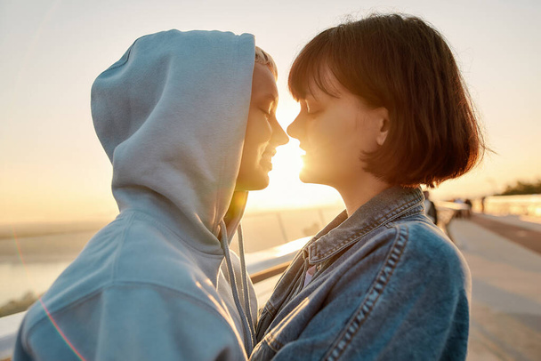 In love. Lesbian couple hugging on the bridge, going to kiss while admiring the sunrise together - Zdjęcie, obraz