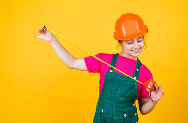 size. teen girl in hard hat and uniform. building and construction. concept of repair. Little girl using a measuring tape. engineer. happy child hold tape measure. kid builder wear helmet - Fotografie, Obrázek