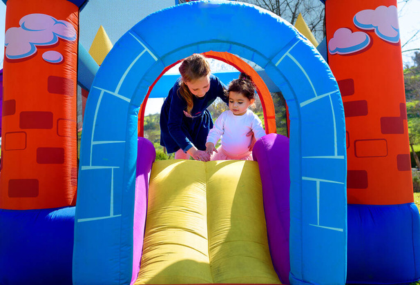 Inflatable castle outdoor at sunny summer day.Two little girls having fun on playground in kindergarten. - Photo, Image