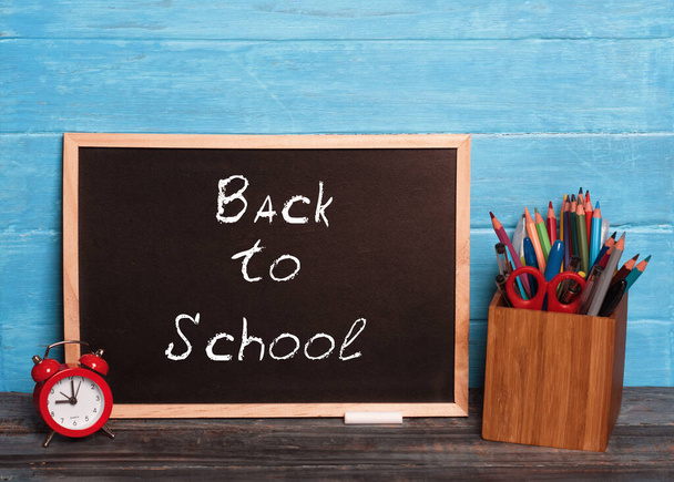 доска с надписью "вернуться в школу", будильник, пенал с ручками - Фото, изображение