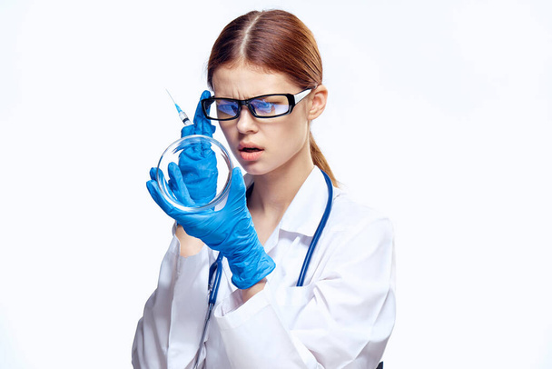 médico mujer en guantes azules con estetoscopio enfermera con gafas inyección jeringa laboratorio luz fondo - Foto, Imagen