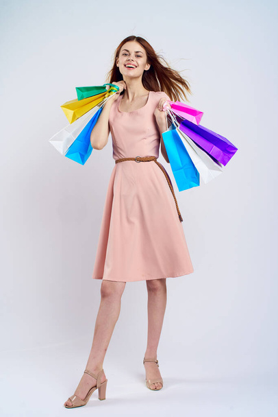 nice girl in a pink dress with shopping bags in her hands in full growth on a light background indoors - Photo, Image