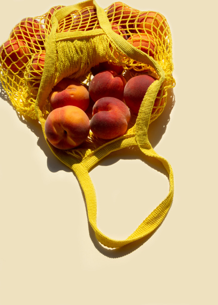 Крупный план спелые персики в сетку мешок или струны мешок на светло-желтом фоне. Плоский лежал. Ноль отходов. - Фото, изображение