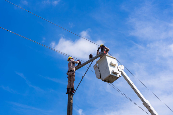 electrician people work installation of high voltage on pole. Engineers working with high voltage hazards - Photo, Image