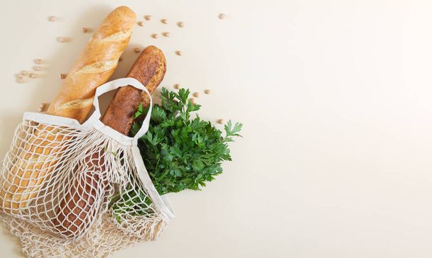 Mesh shopping bag with freshly baked baguettes and parsley top view with copy space - Foto, afbeelding