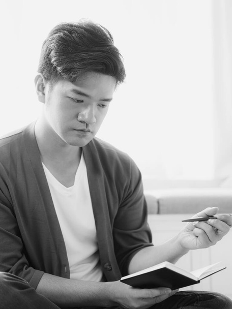 Keresztlábú ázsiai férfi, aki jegyzetfüzetbe ír.. - Fotó, kép