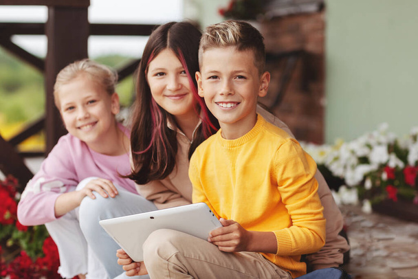 Een groep gelukkige tienerkinderen zit na school op de trap en speelt op een digitale tablet. Moderne kinderen, - Foto, afbeelding
