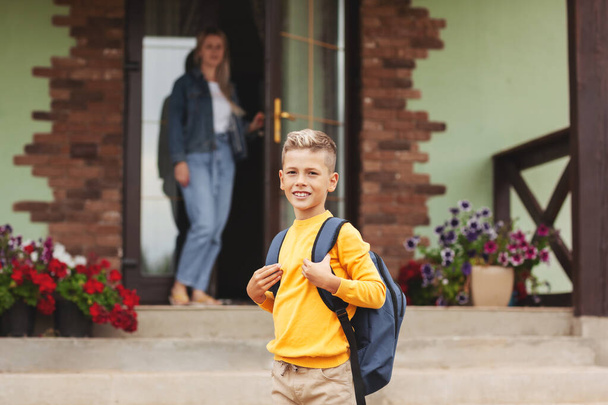 Mom, standing at the door near her house, escorts her son to school, - Valokuva, kuva