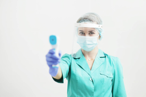Γυναίκα γιατρός ή νοσοκόμα με προστατευτική μάσκα στο νοσοκομείο κρατά το πυρόμετρο στο χέρι. Μέτρα ασφαλείας κατά του κορωναϊού. Πρόληψη Covid-19 έννοια της υγειονομικής περίθαλψης. Στηθοσκόπιο πάνω από το λαιμό. - Φωτογραφία, εικόνα