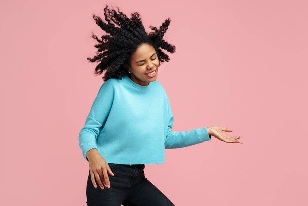Joven afroamericana alegre con brillante sonrisa danza con guitarra invisible sobre fondo rosa. - Foto, imagen