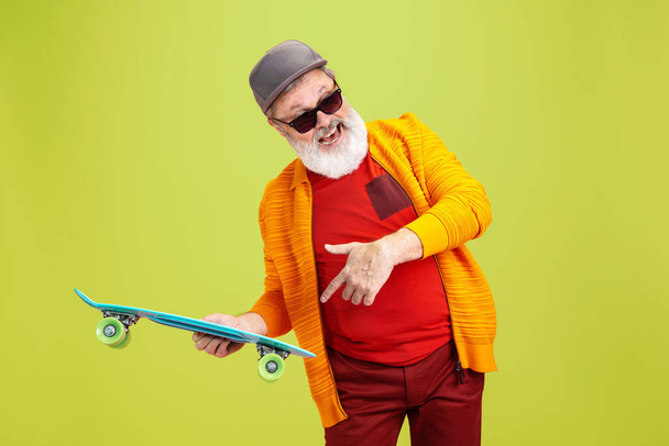 Senior hipster man wearing eyeglasses posing on green background. Tech and joyful elderly lifestyle concept - Foto, imagen