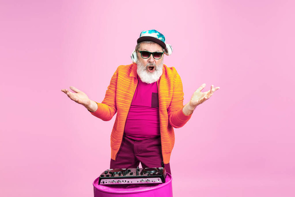 Senior hipster man wearing eyeglasses posing on pink background. Tech and joyful elderly lifestyle concept - Fotó, kép