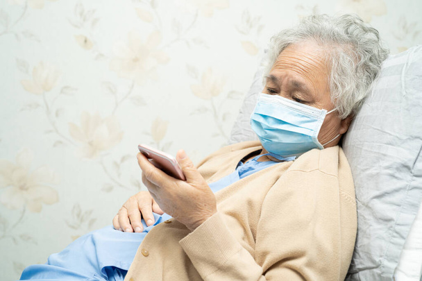 Пациентка азиатского возраста в маске для лица и с мобильным телефоном в больнице для защиты от инфекции безопасности и уничтожения вируса Novel Coronavirus Covid-19. - Фото, изображение