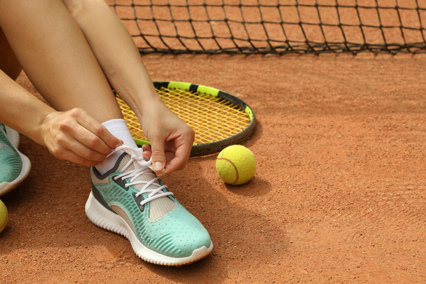 Жінка зав'язує шнурки на глиняному дворі з ракеткою і тенісним м'ячем
 - Фото, зображення