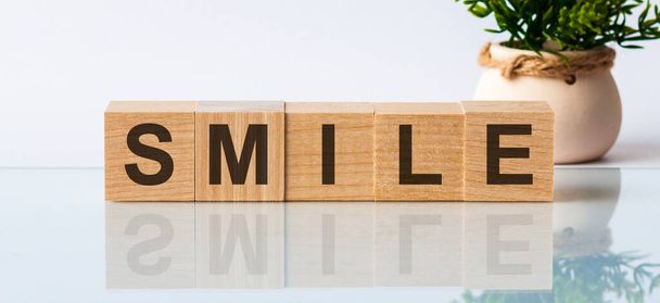 Слово повідомлення SMILE на дерев'яному столі на кубиках з квіткою на фоні
 - Фото, зображення