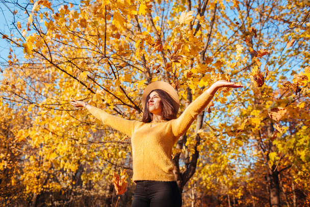 Actividades de temporada de otoño. Mujer lanzando hojas en otoño parkat puesta de sol. Chica joven divirtiéndose al aire libre disfrutando de la naturaleza - Foto, Imagen