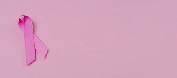 Рожева стрічка раку молочної залози символ обізнаності на рожевому тлі. Панорамне зображення з простором копіювання
. - Фото, зображення