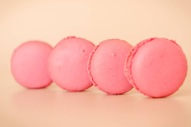 4個のピンクマカロンクッキーとホワイトチョコレートクリームがベージュの背景に転がり - 写真・画像