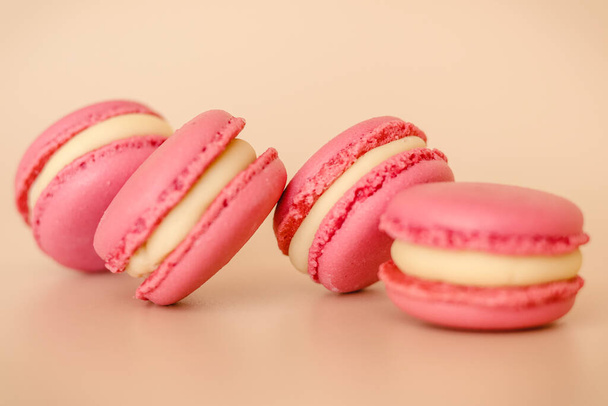 Four pink macaroon cookies with white chocolate cream on beige background - Φωτογραφία, εικόνα