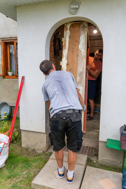 Twee arbeiders ontmantelden de oude deur en namen de oude houten doos mee naar buiten om de nieuwe voordeur verder te installeren.2020 - Foto, afbeelding
