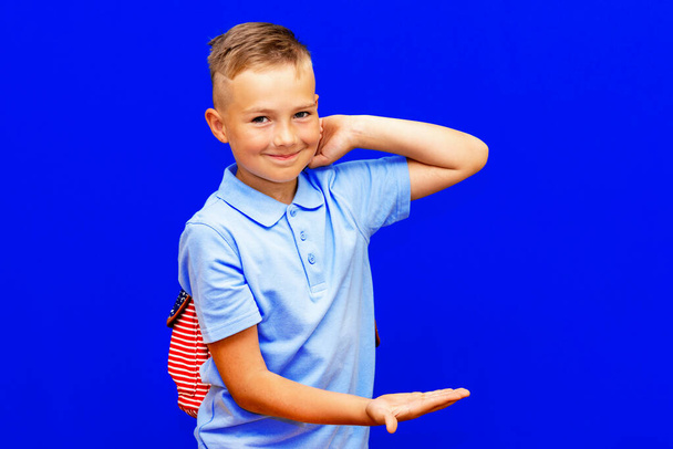 Νεαρός μαθητής σε μπλε t σακίδιο πλάτης πουκάμισο δείχνοντας τα χέρια των χεριών στο χώρο εργασίας που απομονώνονται σε φωτεινό μπλε φόντο - Φωτογραφία, εικόνα