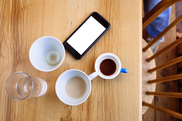 Tazas de café sucias, capuchino y un vaso de agua están sobre una mesa de madera. Junto a las copas hay un teléfono. Descanso. Puesta plana - Foto, imagen