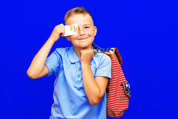 Portrait of school boy in blue t shirt uniform backpack hold in hand credit bank card isolated on bright blue background children studio portrait. - Fotó, kép