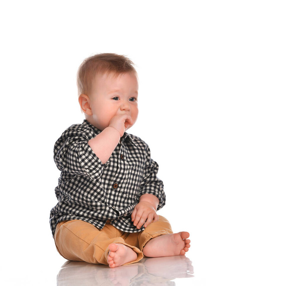 Baby boy in beige pants and a checkered shirt sitting on a white background. - Foto, imagen