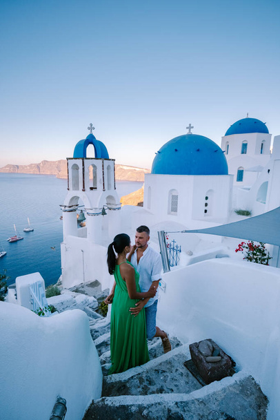 Santorini Grecia, pareja joven en vacaciones de lujo en la isla de Santorini viendo el amanecer por la iglesia de cúpula azul y el pueblo encalado de Oia Santorini Grecia durante el amanecer, hombres y mujeres en - Foto, Imagen