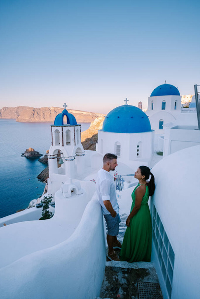 Santorini Griekenland, jong stel op luxe vakantie op het eiland Santorini kijken naar zonsopgang door de blauwe koepel kerk en witgekalkte dorp Oia Santorini Griekenland tijdens zonsopgang, mannen en vrouwen op - Foto, afbeelding