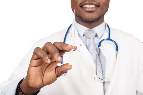 medico maschio in piedi in occhiali con stetoscopio sul collo e siringa sorridente, pronto a dare cure mediche al paziente. - Foto, immagini