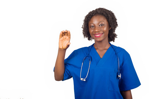 młoda pielęgniarka stojąca w bluzce ze stetoskopem na szyi pokazującym dłoń uśmiechniętą do kamery. - Zdjęcie, obraz
