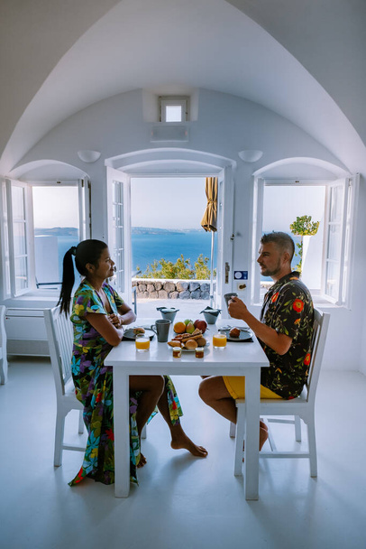 breakfast at traditional historical cave house, Santorini Greece, young couple on luxury vacation at the Island of Santorini watching sunrise by the blue dome church and whitewashed village of Oia - Fotó, kép