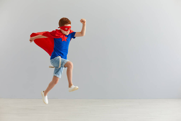 Little boy in a superhero costume jumped on a gray background. Superhero child. Kids costume. - Photo, image