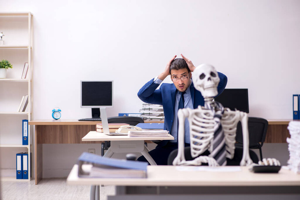 Jonge mannelijke werknemer met skeletten op kantoor - Foto, afbeelding