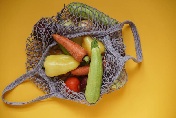 Grijze tas string tas met groenten, courgette, paprika 's, wortelen, bieten, uien geel achtergrond.Oogst uit de tuin verse heldere groenten.Concept nul afval.Bovenaanzicht. Vlakke plaat. - Foto, afbeelding