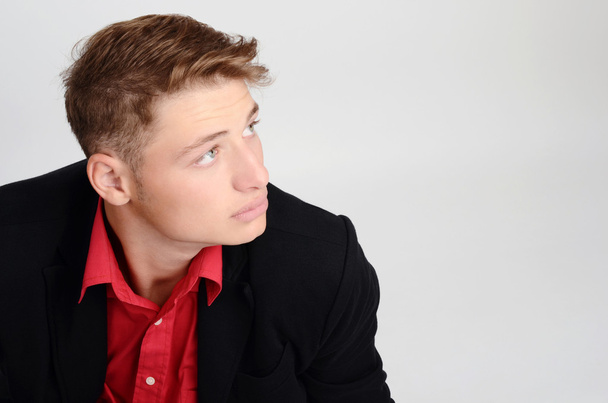 Retrato de um jovem homem de negócios vestindo um terno preto e uma camisa vermelha olhando para o lado. Homem olhando para cima a partir do perfil
. - Foto, Imagem