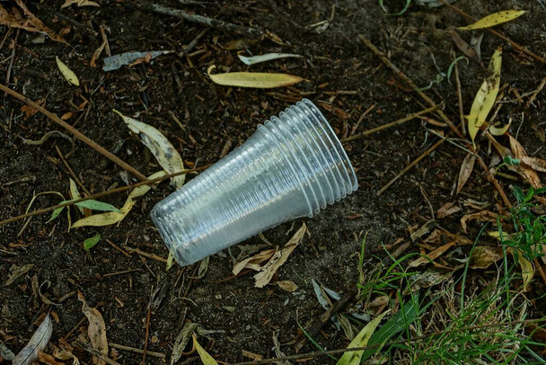 afval van witte plastic bekers op grijze grond en droge bladeren in de natuur - Foto, afbeelding