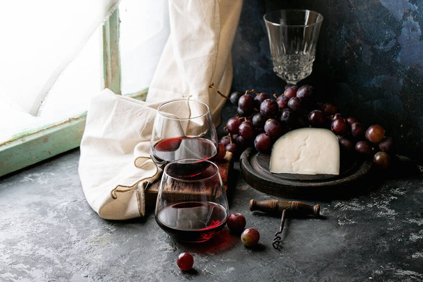 Glass of red wine served with cheese gauda and red grapes over dark texture background - Fotó, kép