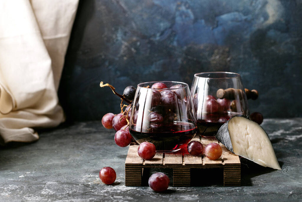 Glass of red wine served with cheese gauda and red grapes over dark texture background. Top view, flat lay. Copy space - Foto, Imagen