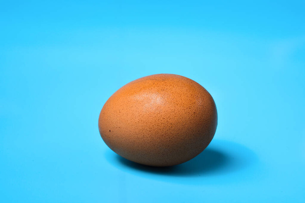 Mavi arka plana yerleştirilmiş bir tavuk yumurtası. - Fotoğraf, Görsel