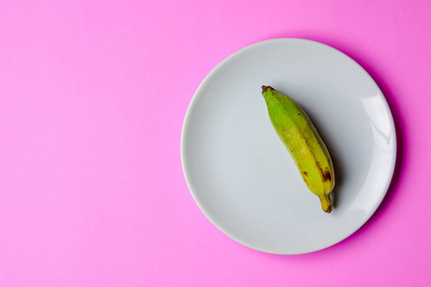 El plátano se coloca en un plato blanco sobre un fondo rosa. - Foto, imagen