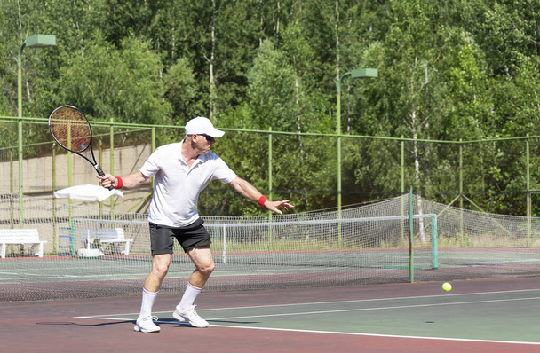 Starší muž v dobré fyzické kondici hraje tenis na venkovním hřišti za slunečného dne - Fotografie, Obrázek