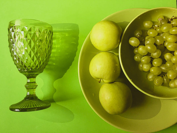 Üç elma ve yeşil bir tabakta bir demet üzüm ve bir şarap kadehi. - Fotoğraf, Görsel