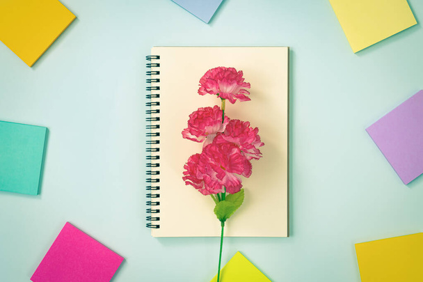 Spirale Notizbuch oder Frühling Notizbuch in ungefütterter Form und mehrfarbige Haftnotiz und rote Blume auf blauem Pastell minimalistischen Hintergrund. Spirale Notizbuch-Attrappe auf Mittelrahmen in Vintage-Ton - Foto, Bild