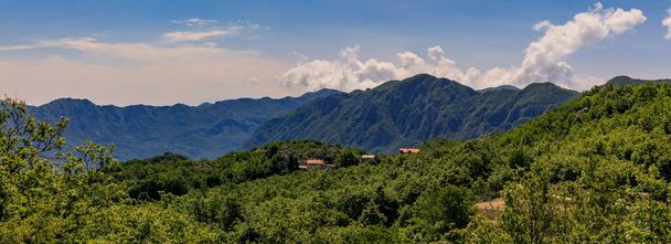 Panoramic view of the rugged mountains with low hanging clouds and a small settlement with red terracotta tile roofs near Novoselje, Montenegro - Foto, afbeelding