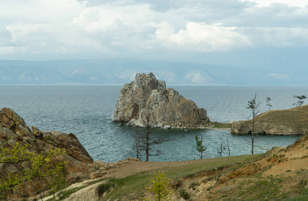 Shamanka Rock op Olkhon. een van de negen heilige plaatsen van Azië. Kaap Burhan. rots bestaat uit marmer en kalksteen, soms overvloedig met grafietpailletten. landschap van het Siberische Baikal meer. - Foto, afbeelding