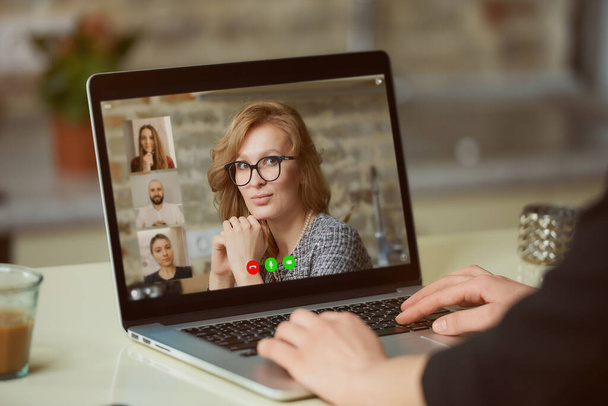 Uma vista do ecrã de um portátil sobre o ombro de uma mulher. Uma senhora está discutindo negócios com seus colegas em um briefing on-line em um computador em seu apartamento. Um estudante em uma reunião de vídeo em um computador. - Foto, Imagem